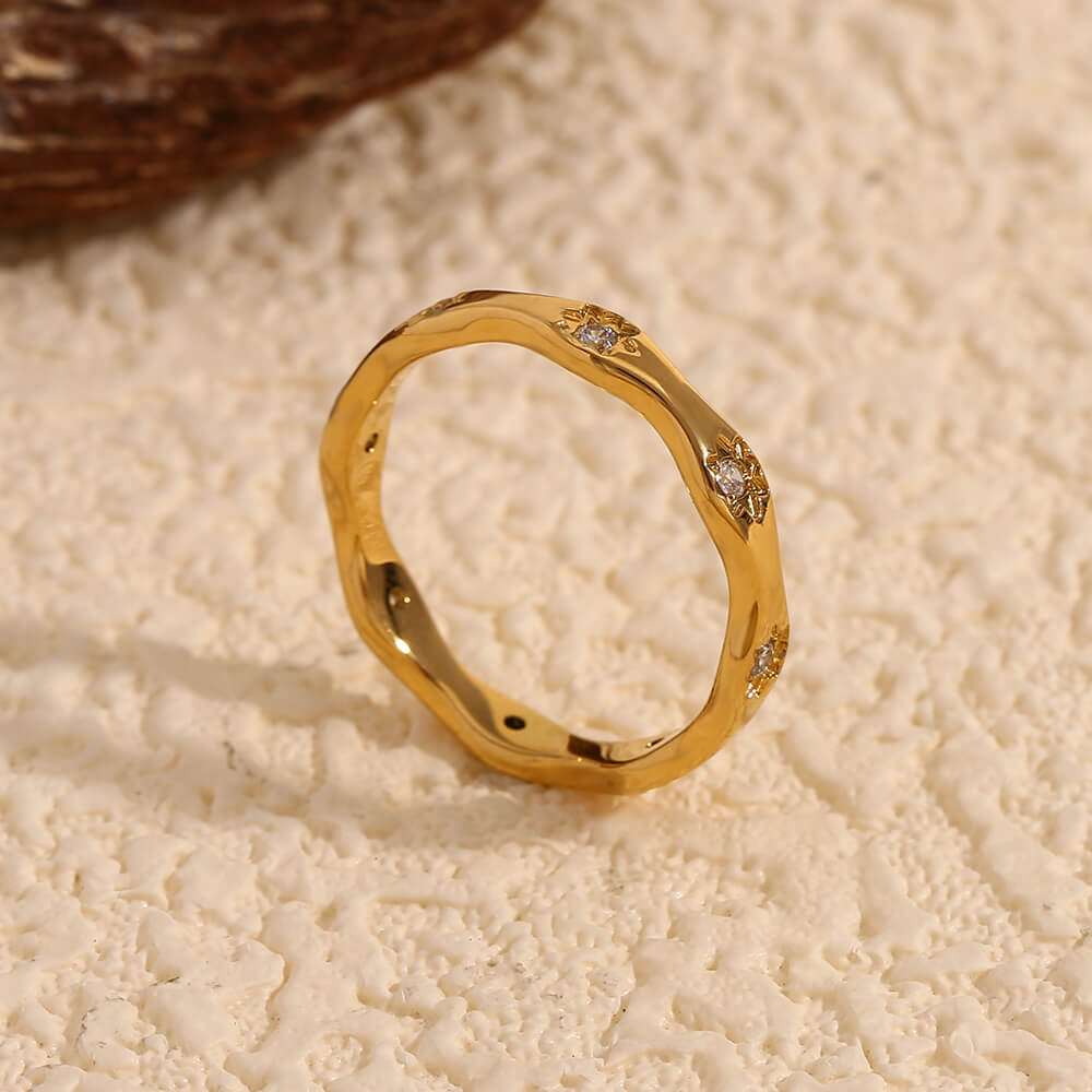 Gold ring band with CZ stones on beige background.