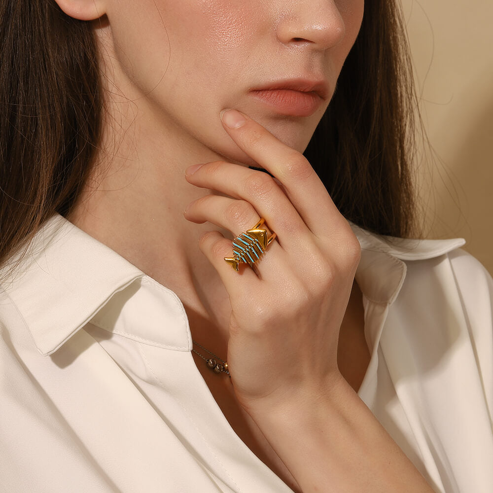 Close-up of a person wearing a gold ring with blue enamel, set against a neutral background.