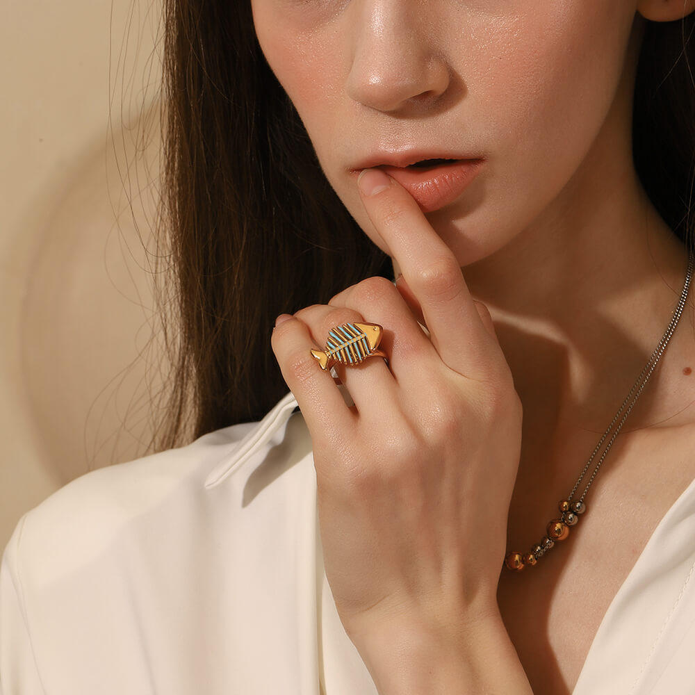 Close-up of a woman wearing a gold fish-shaped ring on her finger, with a neutral background.