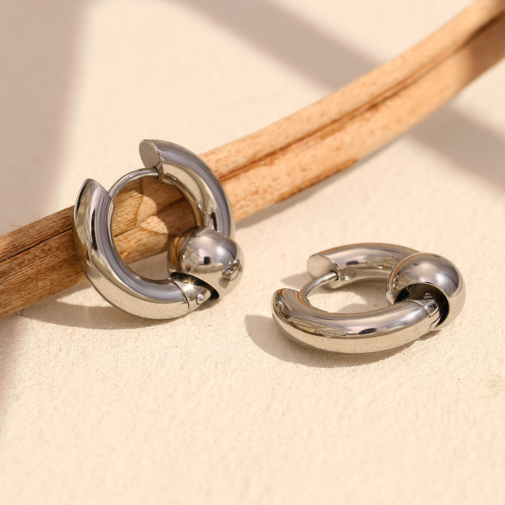 Silver hoop earrings on a wooden stick against a beige background.