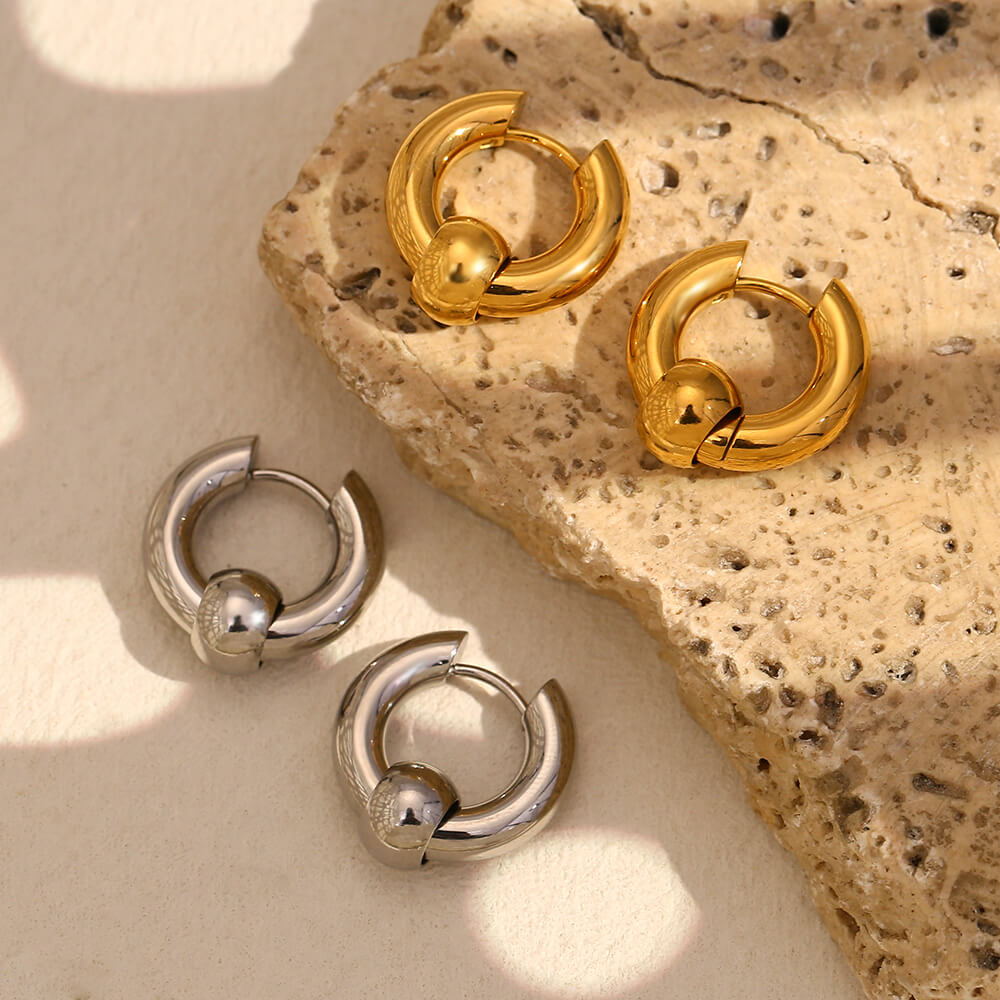 Gold and silver hoop earrings on a textured stone surface.