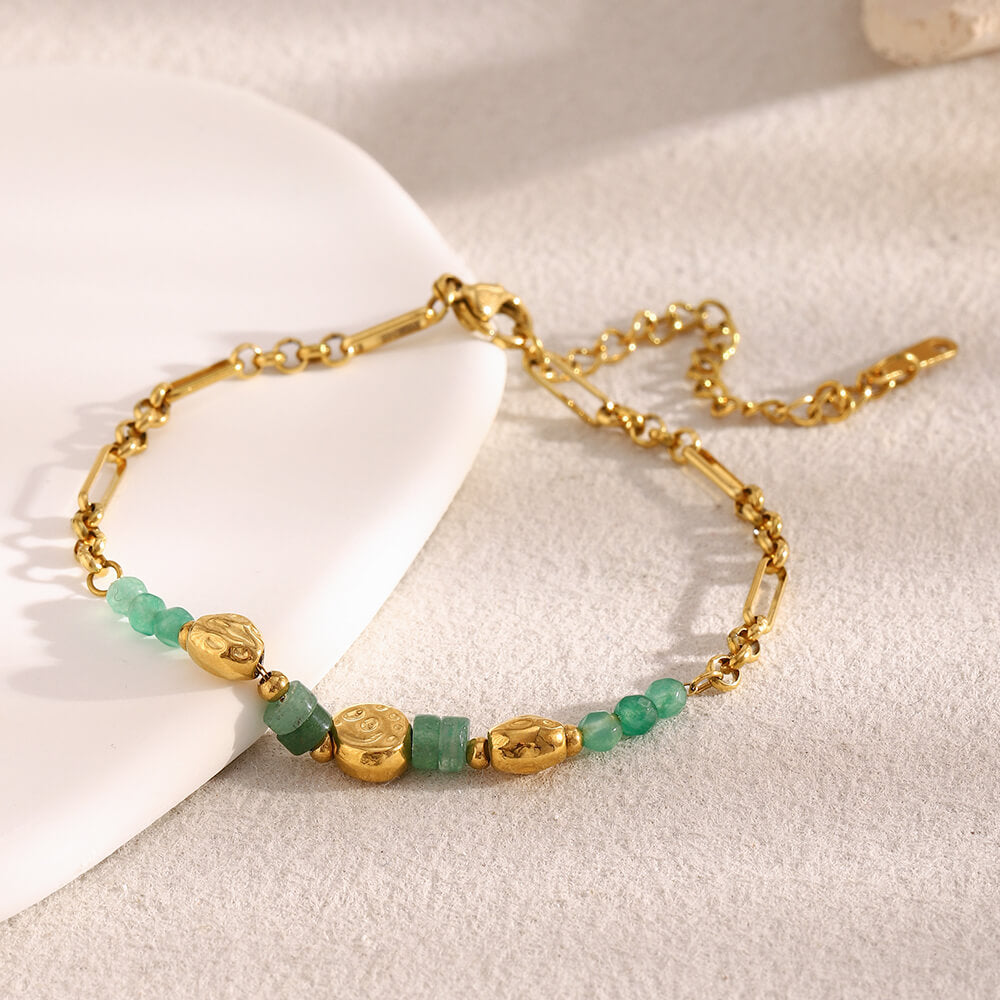 Gold bracelet with green beads on a light background.