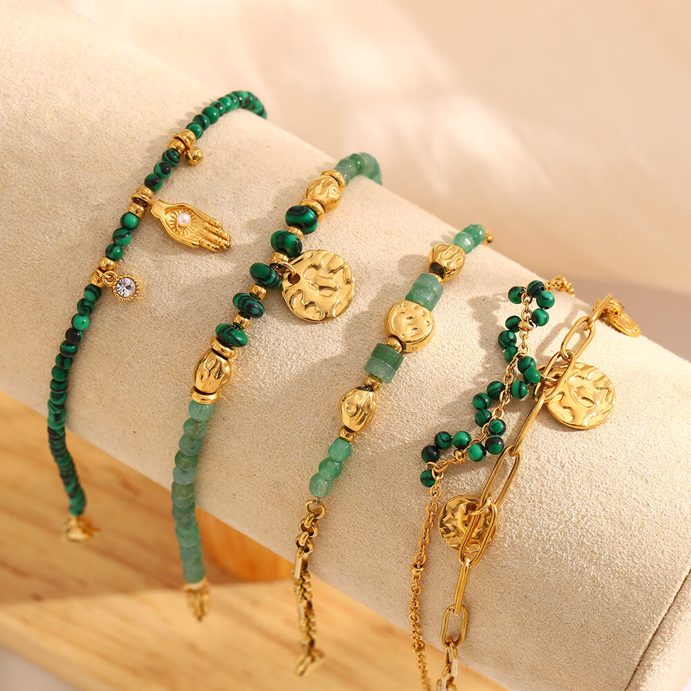 Green beaded and gold bracelets on a beige surface.