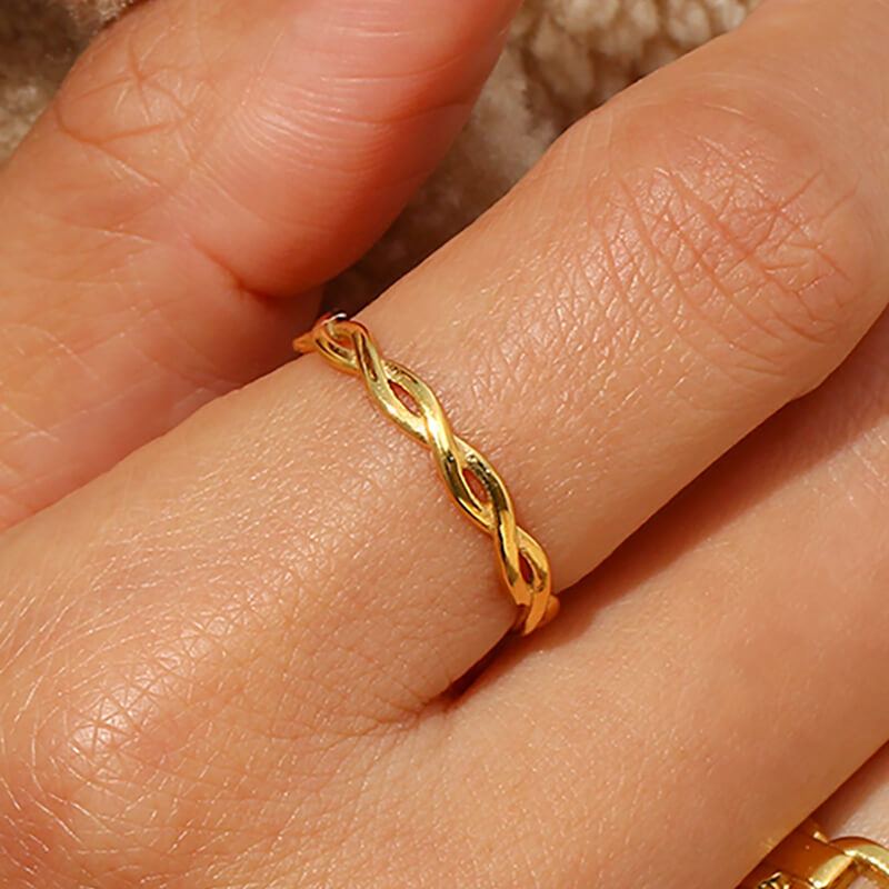 Gold twisted ring on a finger with a neutral background.