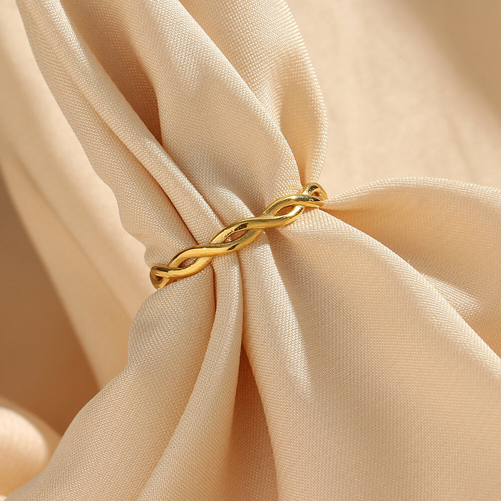 Gold ring with a twisted design on beige fabric.