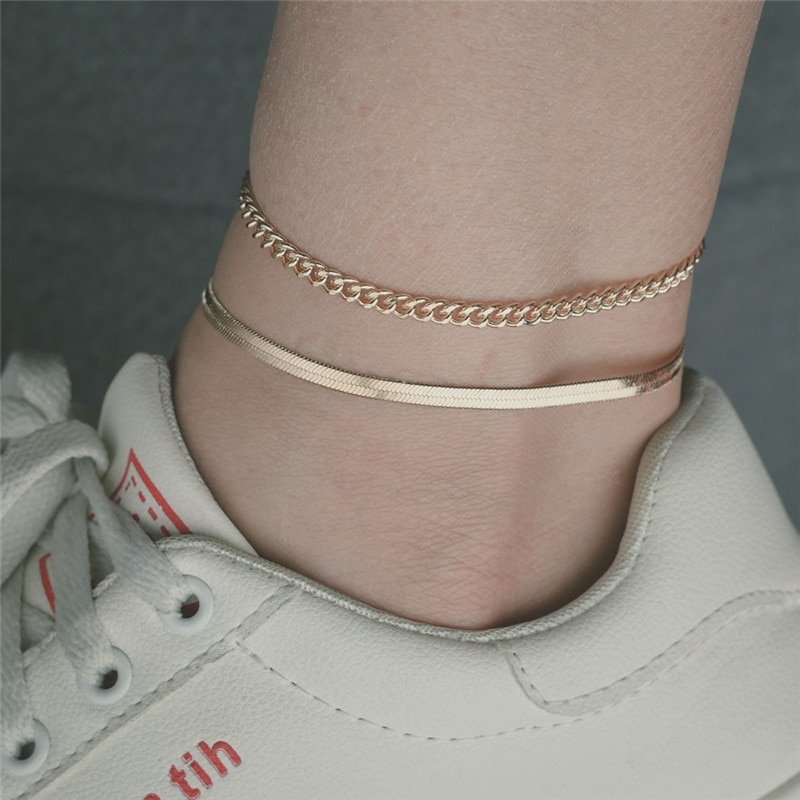 A woman wearing two gold anklets.