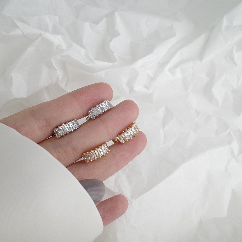 A woman holding gold and silver CZ Baguette Huggies in hand.