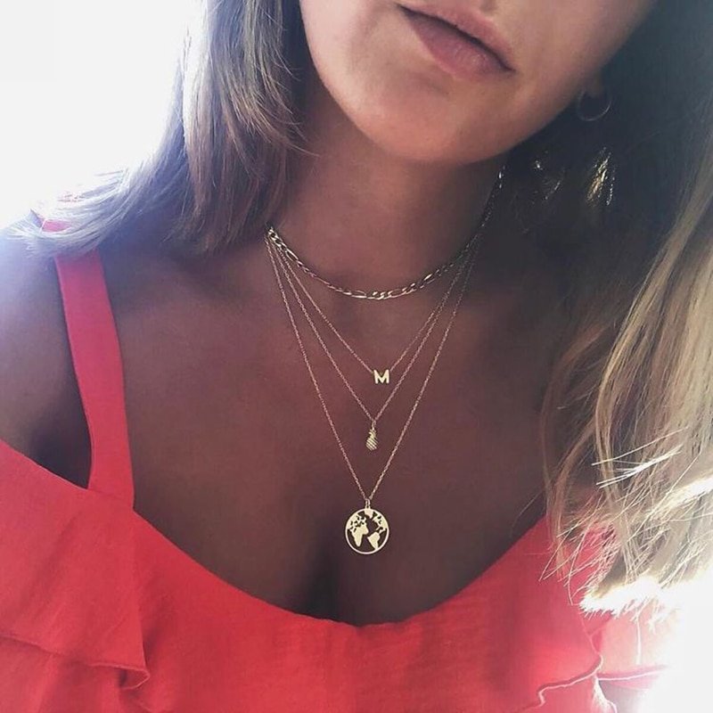 A womn wearing a gold monogram necklace with other gold jewelry.