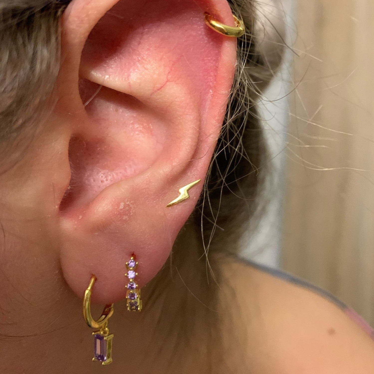 A woman wearing gold hoops with purple stones.