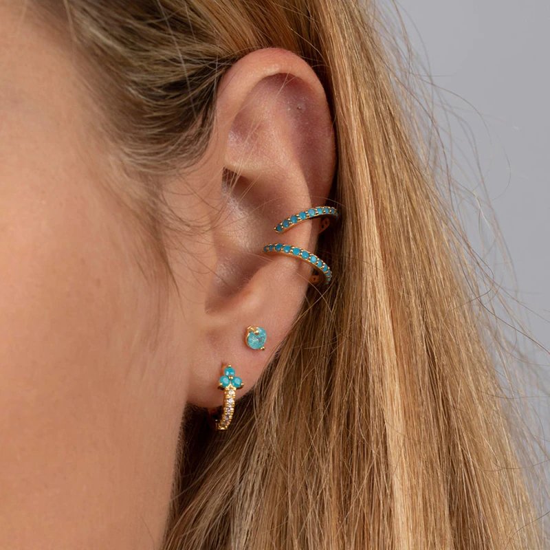 A model wearing multiple gold earrings with turquoise stones.